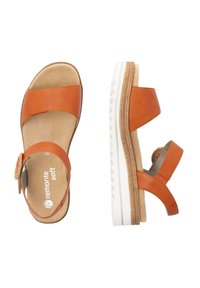Sandales en cuir orange avec deux larges brides, un accent tressé sur le côté et une semelle blanche texturée. Semelle intérieure douce pour le confort.