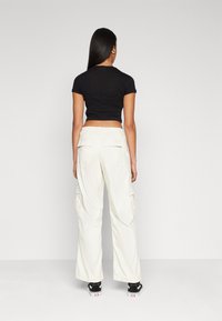Svart kortermet crop-top kombinert med kremfargede cargo-bukser med sidelommer. Modellen har på seg svart og hvite joggesko.