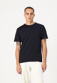 Navy blue cotton t-shirt with short sleeves, standard crew neckline, and relaxed fit. Model stands against a plain white background.