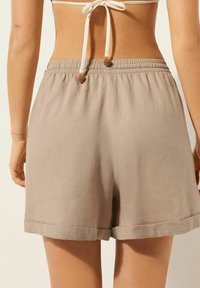 Beige linnéshorts med elastisk midja, med uppvunna fållar och dekorativa snören. Tyget har en mjuk yta.