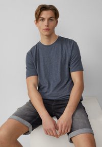 Herren T-Shirt in Dunkelblau mit Rundhalsausschnitt aus weichem Stoff, kombiniert mit hochgekrempelten grauen Denim-Shorts. Schlichtes Design mit kurzen Ärmeln und lockerer Passform.