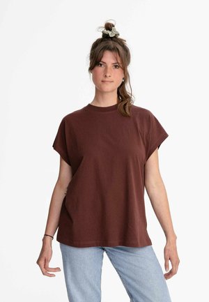 Donkerbruin T-shirt met korte mouwen, gemaakt van zachte stof, met een ronde hals en een relaxte pasvorm. Gecombineerd met lichtblauwe jeans.