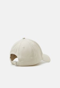 Beige cotton baseball cap featuring a curved visor, adjustable strap at the back, and ventilation holes on the crown.