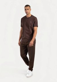 Bruin katoenen T-shirt met korte mouwen, gecombineerd met bruine joggers met zijzakken, afgewerkt met witte sneakers.