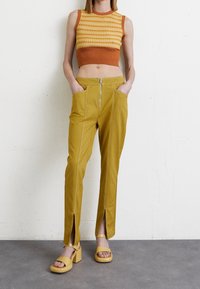 Gula vida byxor med dragkedja fram och sidoflikar, i kombination med en orange och gul strukturstickad kort topp och matchande gula klumpiga sandaler.