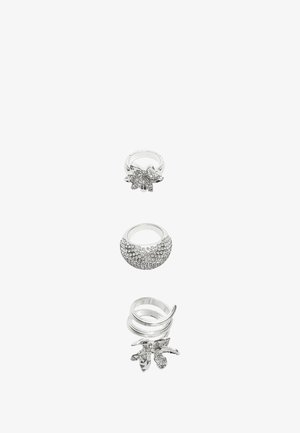 Set van vier zilveren ringen, met verschillende ontwerpen: één met heldere edelstenen, één gladde band en twee met bladvormen.