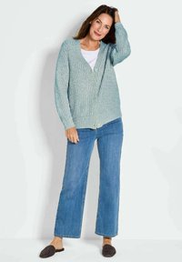 Hellblauer Cardigan mit strukturiertem Strick, V-Ausschnitt und Knopfverschluss, kombiniert mit weit geschnittenen Denim-Jeans und dunklen Slippern.