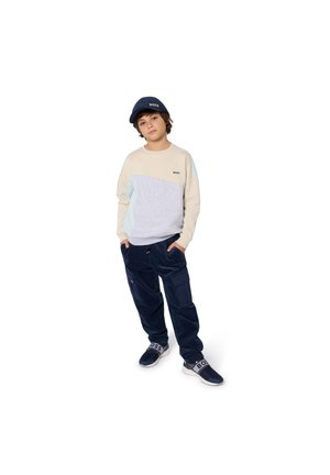 Light beige and gray color-blocked sweatshirt with a logo, paired with dark blue cargo pants. The subject wears a matching cap and sporty shoes.