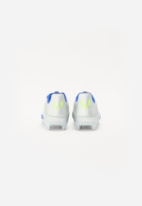 Des chaussures de football avec une tige synthétique argentée, des accents bleus et un logo jaune vif. Elles présentent un talon texturé et des crampons moulés pour une meilleure traction.