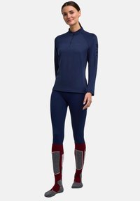 Marineblaues Langarmoberteil mit Viertelreißverschluss, eng anliegende marineblaue Leggings und knielange burgunderfarbene Socken mit grauen Akzenten und Mustern.