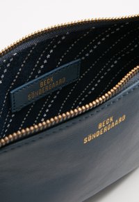 Borsetta in pelle blu con zip dorata, foderata in tessuto con stelle bianche disposte in un motivo diagonale. Etichetta del marchio visibile all'interno.