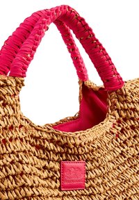 Borsa di paglia tessuta con manici in tessuto rosa. Presenta un interno di un rosa brillante e una piccola etichetta con logo in rilievo rosa sul lato.