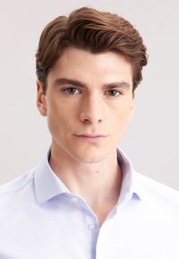 Camicia button-up azzurro chiaro con un sottile motivo a spina di pesce, colletto strutturato e tessuto morbido, indossata da un modello maschile con capelli corti castani.