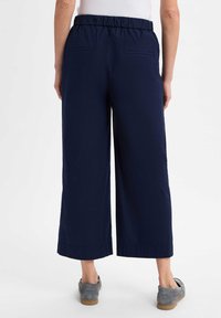 Marinefarbene weite Hose mit einem elastischen Bund und zwei Gesäßtaschen, ausgestattet mit einer glatten Textur und umgeschlagenen Säumen. Kombiniert mit grauen Slippern.