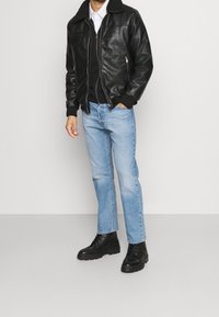 Czarna skórzana kurtka z kołnierzem z owczej skóry, zestawiona z czarnym swetrem, jasnoniebieskimi dżinsami i czarnymi sznurowanymi botkami.