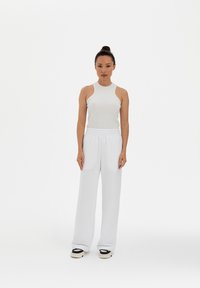 White ribbed tank top with a high neckline, paired with loose white sweatpants and black and white sneakers. Plain background.