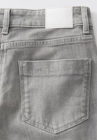 Lichtgrijze denim jeans van achteren gezien, met een enkele achterzak en een wit gestikte rechthoekige merkpatch boven de tailleband.