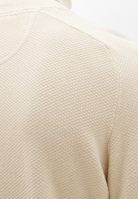 Pull beige texturé présentant un motif en tricot nid d'abeille et un col montant, avec des coutures courbes et un matériau doux et respirant.