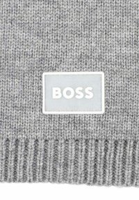 Beanie grigio a maglia con texture a coste. Presenta una patch rettangolare bianca con la scritta "BOSS" in lettere bold.