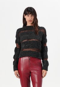 Black knitted sweater with open weave and textured stripes, featuring hints of orange. Paired with red leather high-waisted pants.