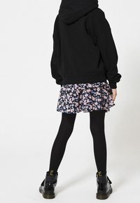 Black oversized hoodie, navy floral ruffled skirt, black tights, and black shiny ankle boots with yellow accents.