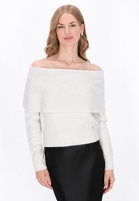Pull blanc avec un design à épaules dénudées, texture côtelée et look superposé. Associé à une jupe noire, avec une finition lisse.