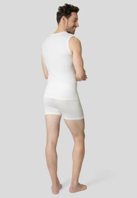 Un débardeur sans manches blanc et un short assorti, fabriqués dans un tissu lisse et extensible. Le modèle se tient de dos, tourné vers le spectateur.
