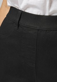 Pantalones de mezclilla negra con una textura suave, que cuentan con una cintura estándar, bolsillo lateral y detalles de costura sutiles.