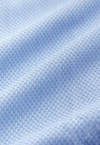 Šviesiai mėlyna medžiaga su tekstūriniu raštu, kuriame matomi maži, iškilę rombo formos elementai, sukuriančius subtilų tinklo efektą. Lygi paviršiaus faktūra.