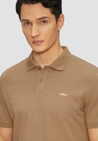 Camisa polo marrón con cuello, dos botones y un pequeño logo bordado de s.Oliver en el lado izquierdo del pecho. Material de algodón texturizado.