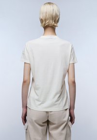 Korte mouw, crèmekleurig t-shirt, gemaakt van zacht katoen. Heeft een ronde halslijn en een klein logo-opdruk op de linker mouw.
