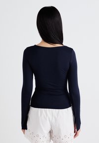 Haut à manches longues navy avec une coupe ajustée, un col rond et des fentes sur les côtés, associé à un short blanc avec des motifs en œillet.