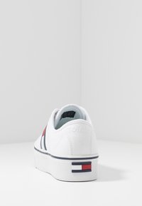 Sneaker bianca in tela con suola a piattaforma, caratterizzata da strisce blu navy e rosse e "TOMMY" impresso sul tallone. Accent logo in gomma sul retro.
