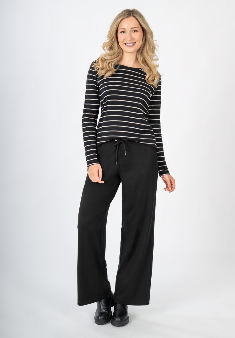 Zwart-wit gestreepte longsleeve top, gedragen met zwarte wijde broek met een trekkoord in de taille. Het model draagt zwarte enkellaarsjes.