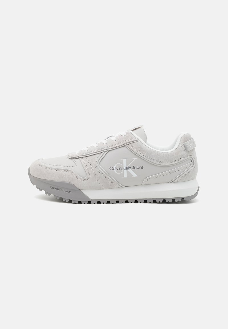 Pantofi sport albi din materiale din suede și sintetice, având o talpă texturată, un design cu șireturi și un logo pe lateral.