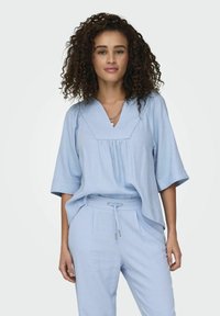 Maglietta azzurro chiaro, in fit rilassato, con maniche corte e scollatura a V, abbinata a pantaloni coordinati con coulisse per la vita regolabile.