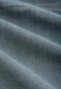 Weicher blauer Denim-Stoff mit sichtbarer Webstruktur und sanften Falten, die diagonale Schatten und Highlights erzeugen.