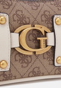 Brązowa torebka materiałowa w wzory z zapięciem w złotym kolorze, kremowymi skórzanymi akcentami i złotymi ćwiekami wzdłuż paska. Teksturowana powierzchnia.