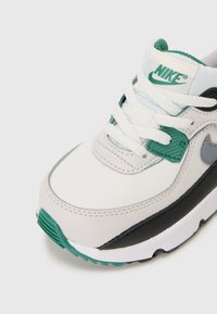 Basket de Nike avec une tige en cuir blanc, des accents noirs, des détails verts et des lacets blancs. Présente une languette texturée et un col rembourré.