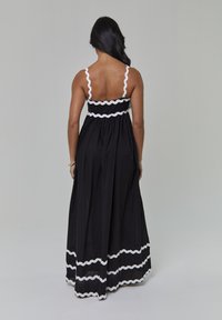 Czarna długa sukienka maxi z białą falbanką ric-rac na górze i na dole, z cienkimi ramiączkami i luźną sylwetką. Gładka tkanina i marszczona talia.