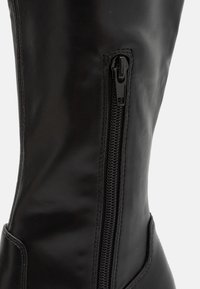 Botte noire haut de genou en matériau synthétique lisse, dotée d'une fermeture éclair sur le côté et d'un design ajusté pour un port sûr.