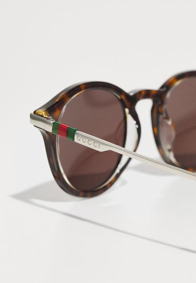 Lunettes de soleil rondes écaille avec verres foncés et branches argentées ornées de rayures vert-rouge-vert et logo Gucci.