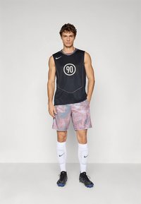 Must musta sportlik topp, millel on ümmargune "90" logo, koos mustriga hallide lühikestega, millel on punased aktsendid. Valged põlvekõrged sokid ja mustad jalanõud.