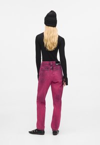 Uska crna rebrasta majica dugih rukava, uparena s visokim rozim trapericama s istrošenom teksturom i stražnjim džepovima. Dodaci: crna kapa.