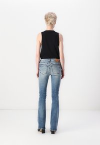 Jeans din denim evazați, de culoare albastru deschis, cu un finisaj decolorat, asortați cu un top negru fără mâneci. Partea din spate prezintă o etichetă din piele cu marcaj.
