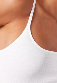 White cotton tank top with thin straps, featuring a ribbed texture and a close-cut design, accentuating the shoulder and neckline.