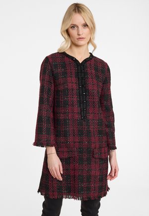 Red and black plaid tunic with a textured finish, featuring a fringed hem, long sleeves, and a buttoned front closure.