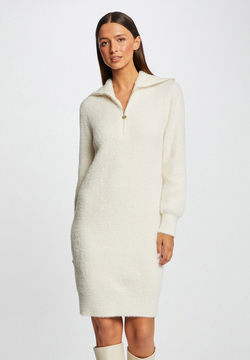 Abito maglione color crema realizzato in materiale peloso, con colletto a mezza zip e maniche lunghe, dalla vestibilità ampia e orlo svasato.