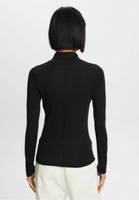Svart långärmad polotröja med en figurvänlig silhuett och slät textur, med en sömlös baksida och sträckbart material.