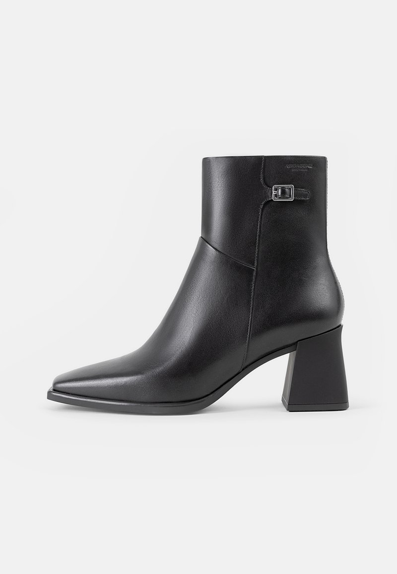 Bottine en cuir noir à bout pointu, talon bloc et petite boucle latérale sur fond blanc uni.
